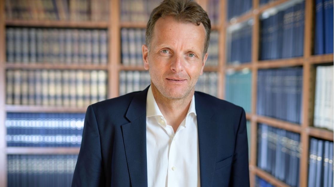 Portraitfoto von AIF-Vorstand Thomas Reiche im weißen Hemb und dunkelblauen Sakko, im Hintergund Bücherregale