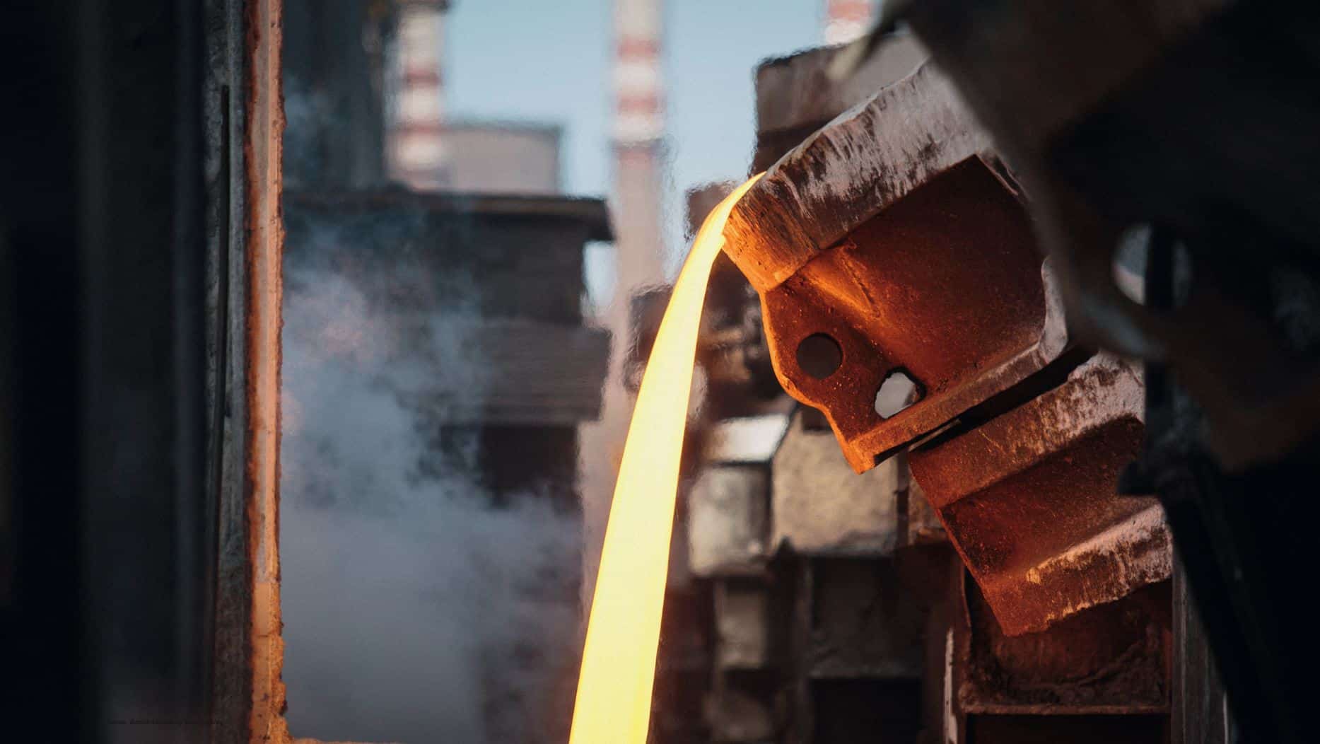 Glühender flüssiger Stahl wird ausgegossen, im Hintergrund industrielle Schornsteine, © Canva, Bence Szemerey von Pexels