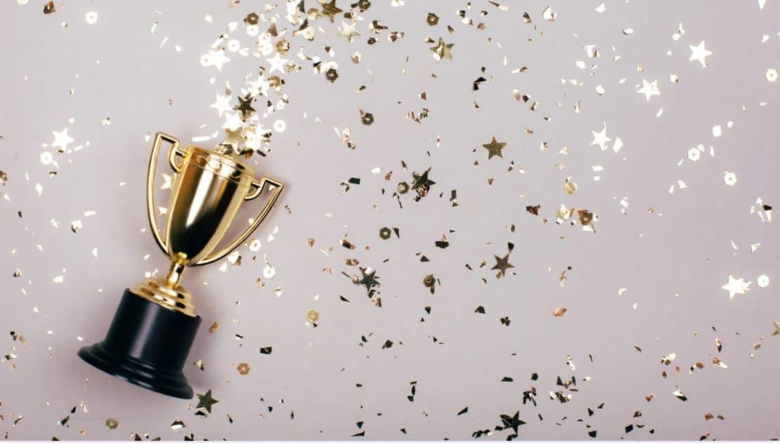 Goldener Pokal, aus dem goldene und weiße Flitterteile fliegen, auf grauem Untergrund; Copyright Canva Getty Images, efetova