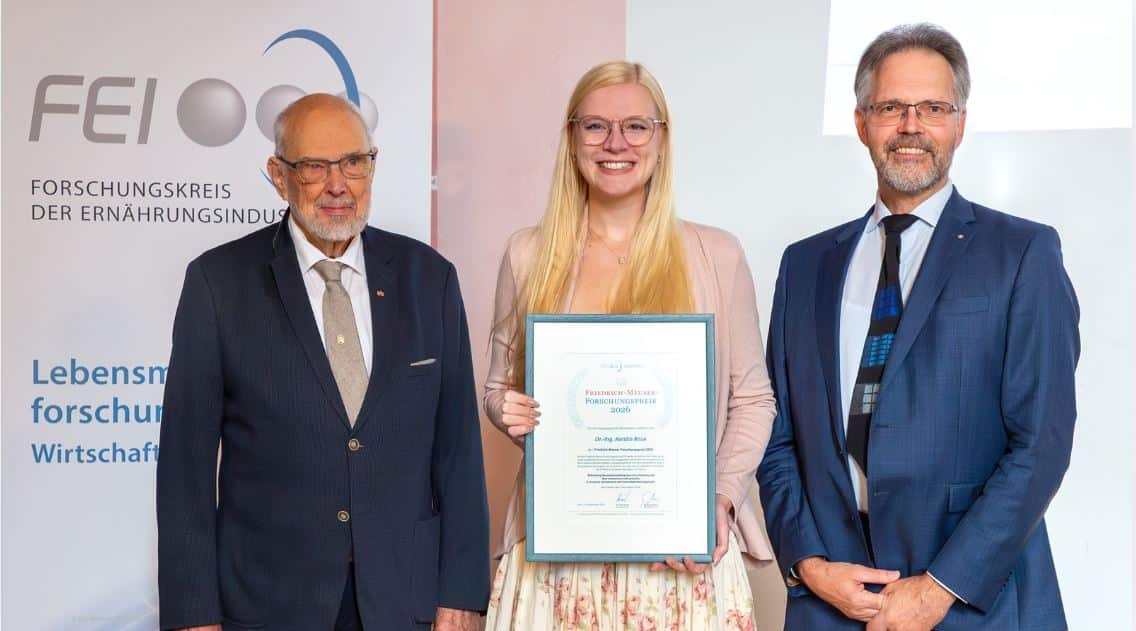 Eine junge blonde Frau mit Urkunde, umrahmt von zwei älteren Herren im Anzug, im Hintergrund Schriftzug des Forschungskreises der Ernährungsindustrie (FEI), © FEI | Michaela Wohlleber